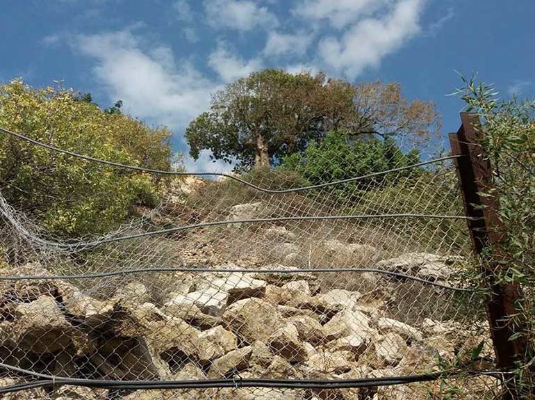 Rocks that have already fallen down the hillside are held back by wire fending