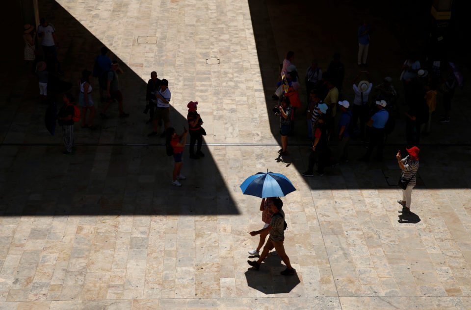 Tourists seek shelter from the sun while others walk by with an umbrella, as a heatwave hits Europe, in Valletta, Malta, June 26, 2019.  REUTERS/Darrin Zammit Lupi