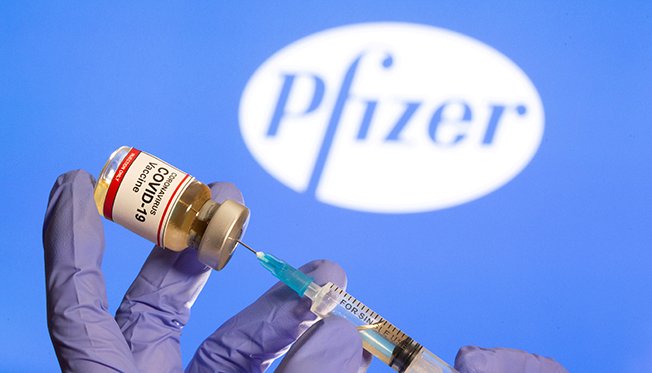 File Photo: A Woman Holds A Small Bottle Labeled With A "coronavirus Covid 19 Vaccine" Sticker And A Medical Syringe In Front Of Displayed Pfizer Logo In This Illustration