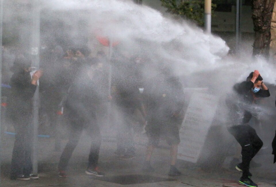 protesters and activists are sprayed with a water cannon during a rally against corruption and covid 19 restriction measures, in nicosia
