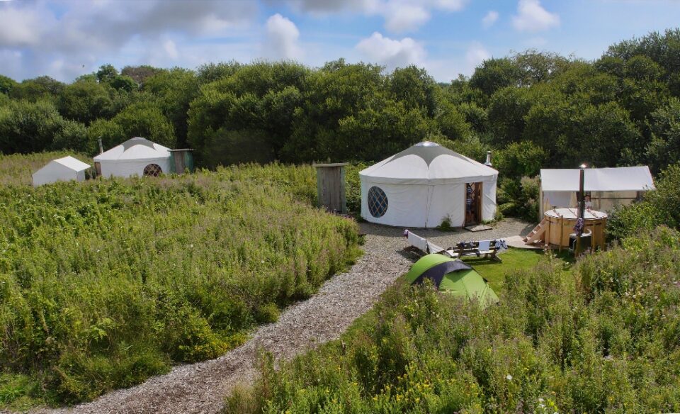 a glamping village with semi permanent yurts, gravel paths, and a hot tub