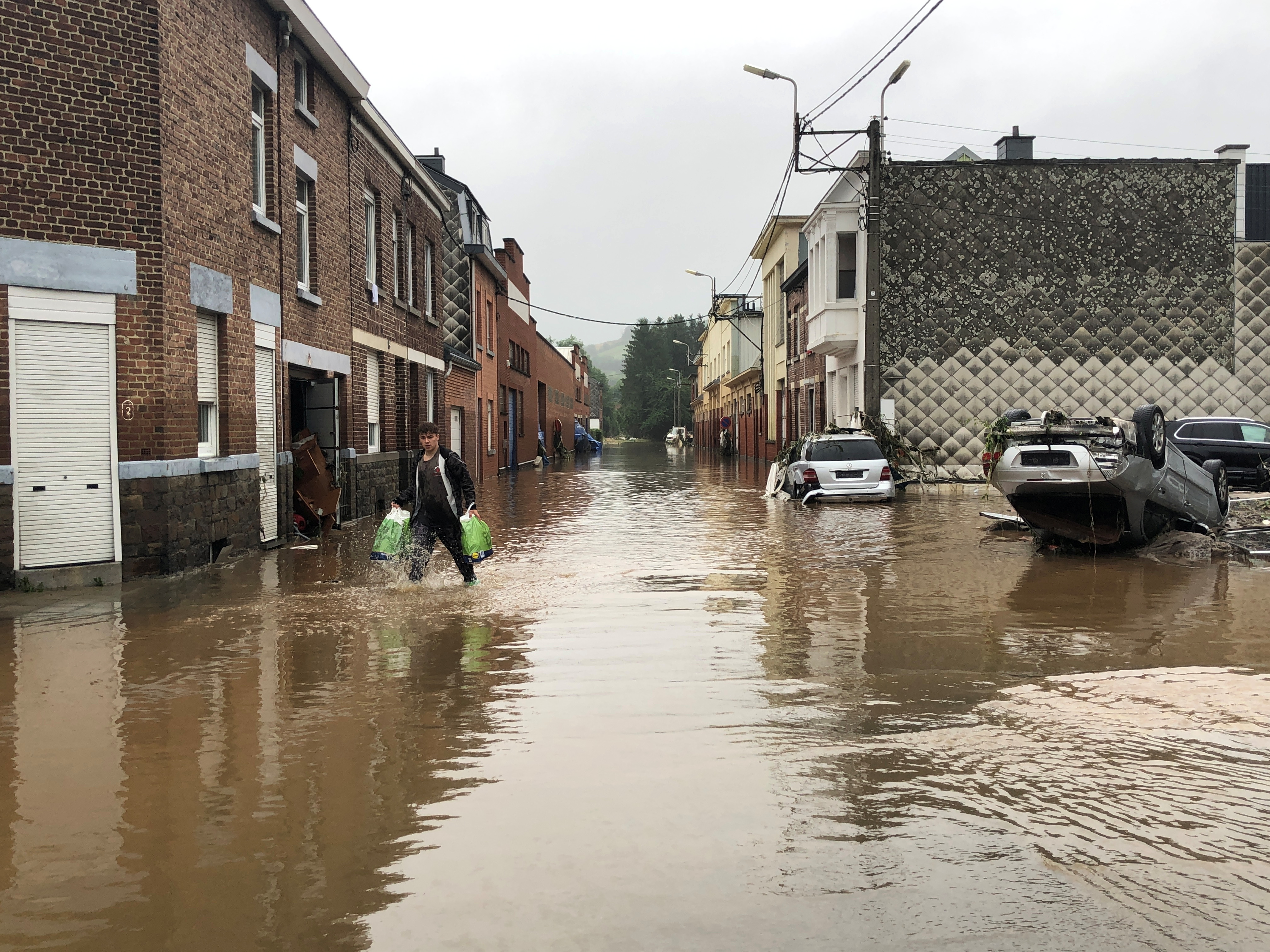 a man walks past partially submerged cars on a flooded street in pepinster