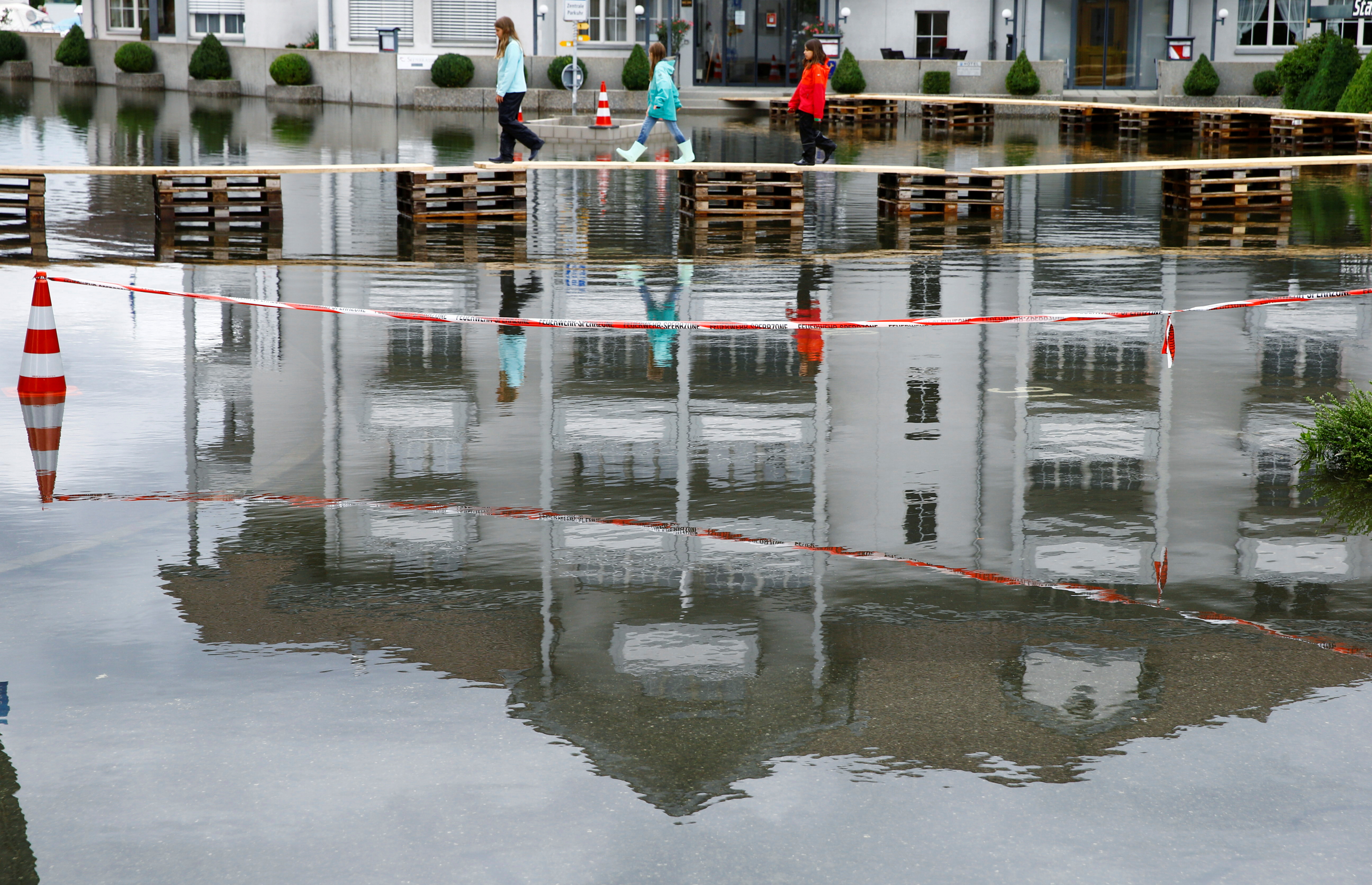 girls walk on a temporary footbridge on the village square flooded after torrential rain in stansstad