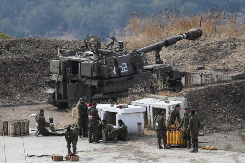 israeli soldiers stand next to an artillery unit on the israeli side of the border with lebanon