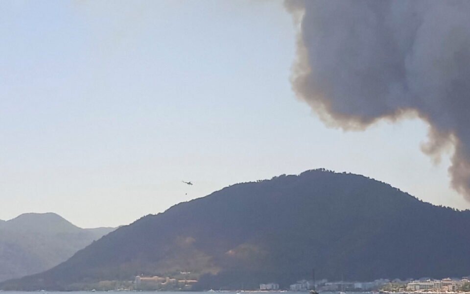 a helicopter throws buckets of water to put out flames in the coastal resort of marmaris