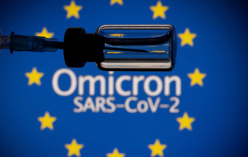 a vial and a syringe are seen in front of a displayed eu flag and words "omicron sars cov 2" in this illustration taken