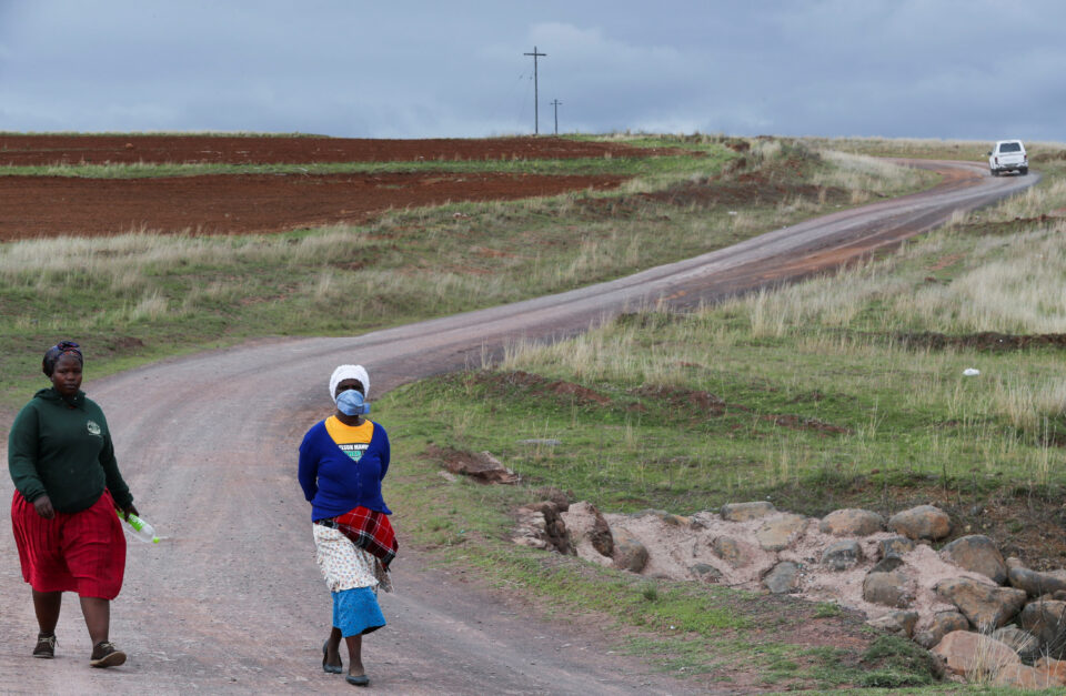 women walk on a dirt road carrying firewood in qumanco