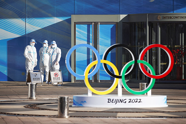 workers in ppe stand next to the olympic rings inside the closed loop area near the national stadium in beijing