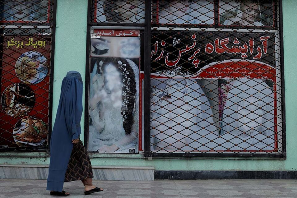 file photo: a woman walks past a shop with defaced pictures of women in kabul