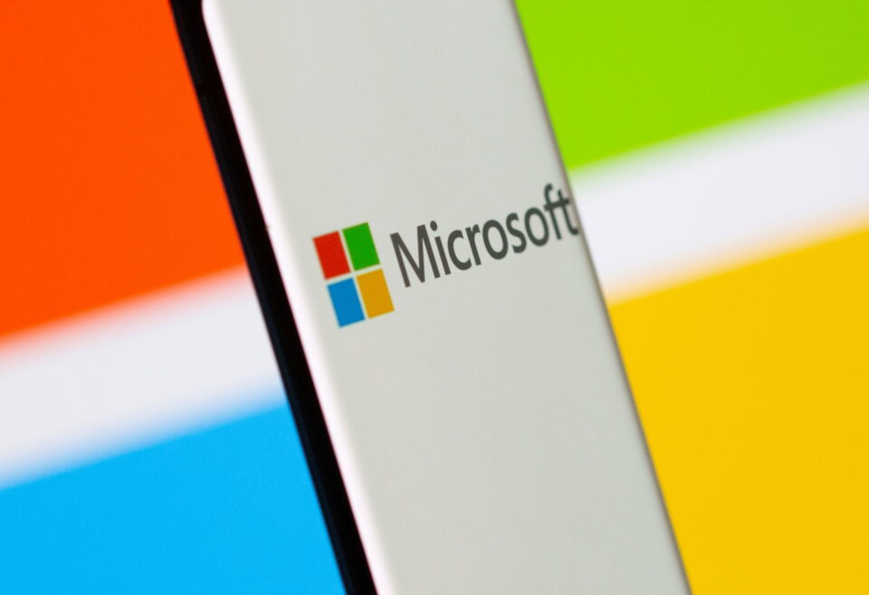 smartphone is seen in front of microsoft logo displayed in this illustration taken