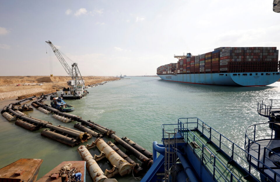 shipping container passes through the suez canal as excavators work on expanding it, in suez