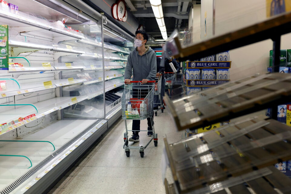 a customer wearing a mask shops in front of partially empty shelves at a supermarket in hong kong