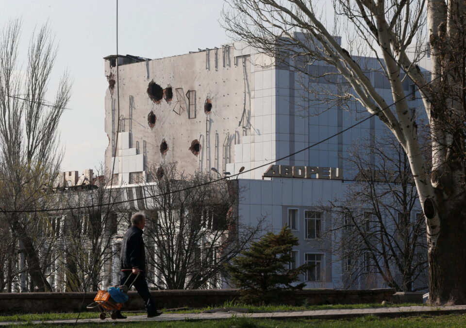 a local resident walks past the damaged palace of culture in mariupol