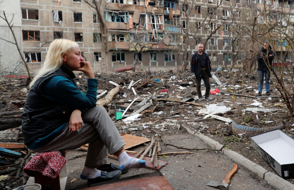 people gather in a courtyard outside a damaged block of flats in mariupol
