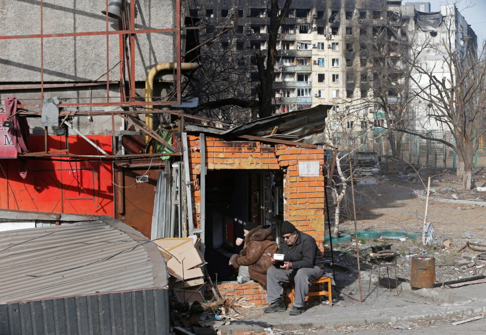 local residents have a meal outside a damaged building in mariupol