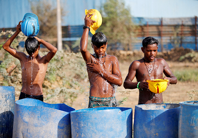 workers use their helmets to pour water to cool off near a construction site on a hot summer day on the outskirts of ahmedabad