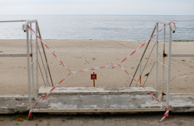 a sign warning people of mines is pictured at a closed off beach, in odesa