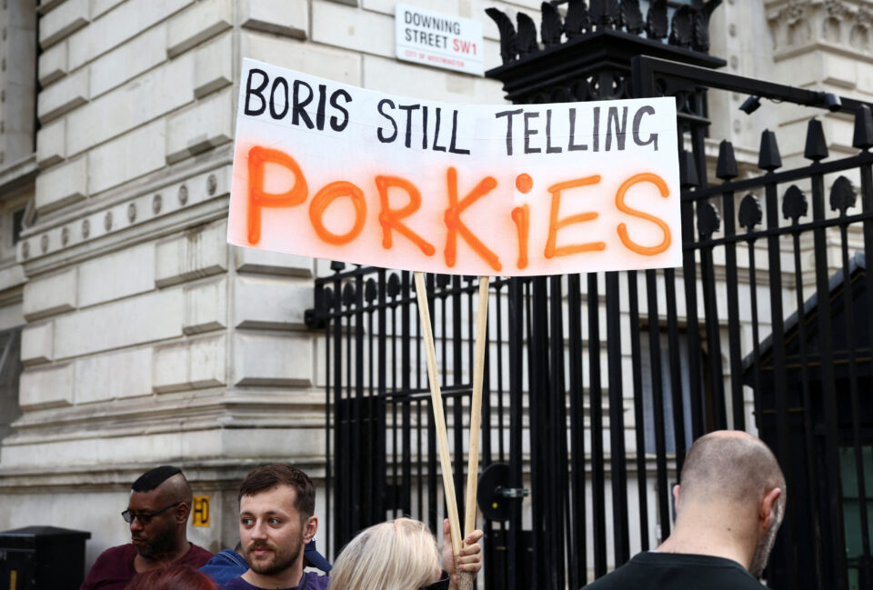 a man holds a sign outside the gate of 10 downing street, in london