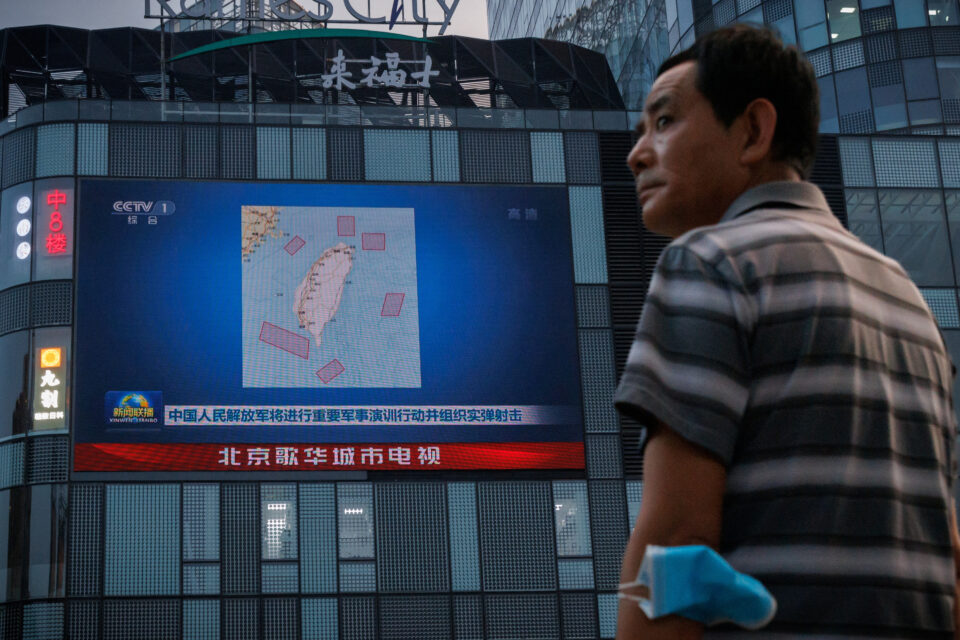 a man stands in front of a screen, showing a news broadcast about joint military operations near taiwan by the chinese people's liberation army's (pla), in beijing
