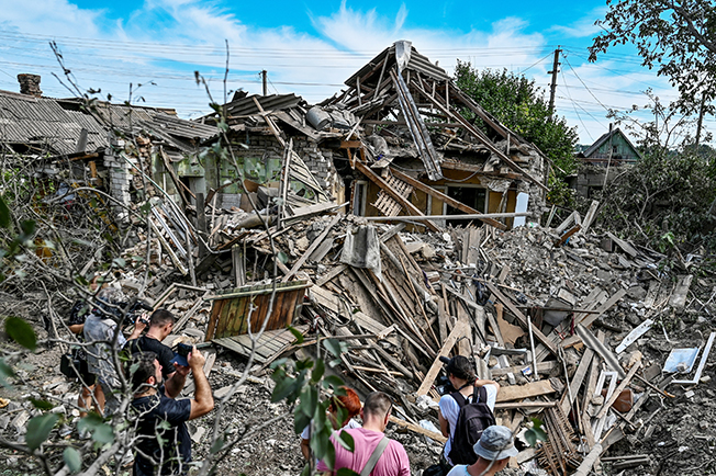 people stand next to a residential house destroyed by a russian missile strike in the settlement of kushuhum