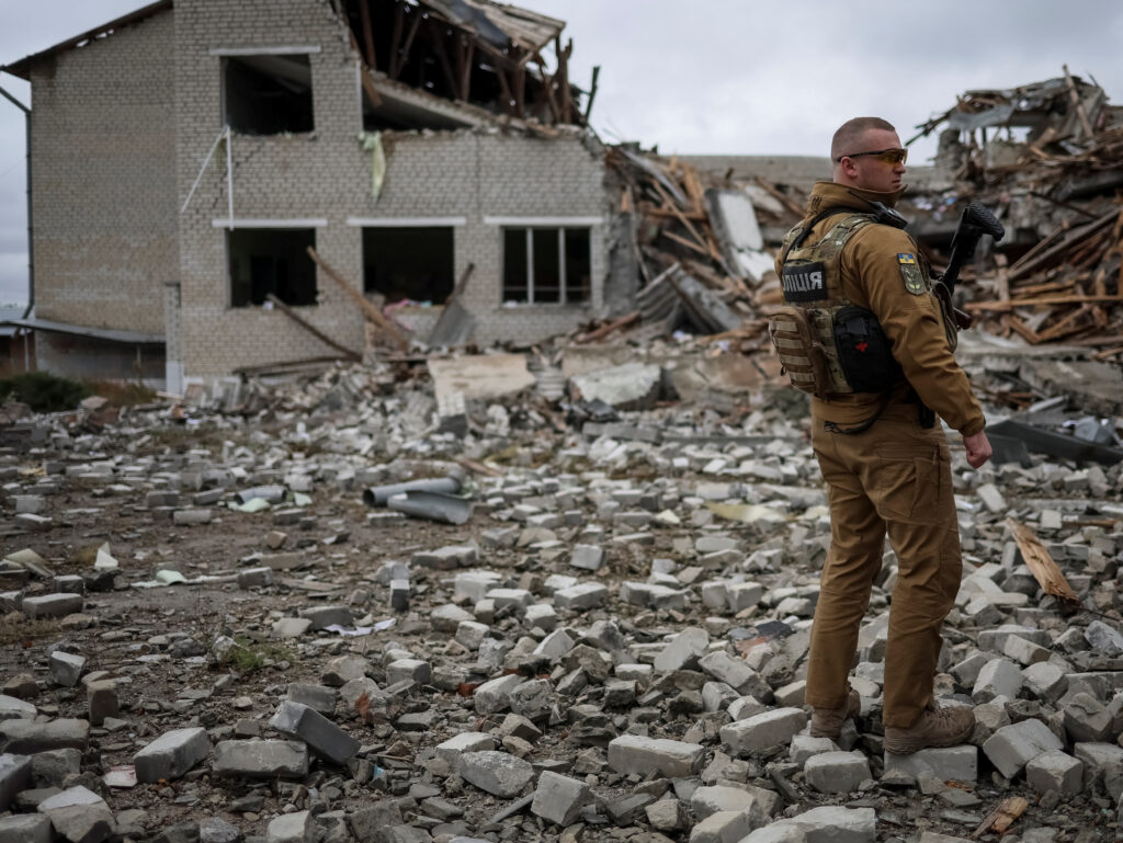 ukrainian police officer stands guard near destroyed school building, in the village of verbivka