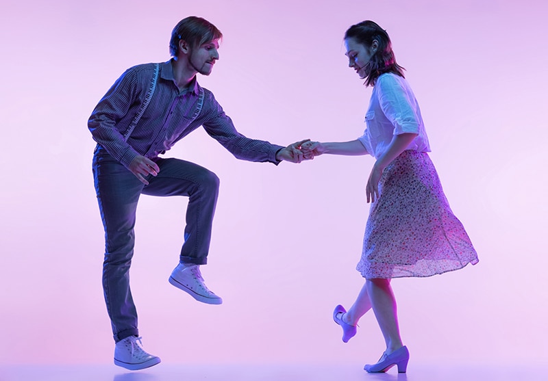 two young people, man and woman, dancing swing isolated over purple background in neon